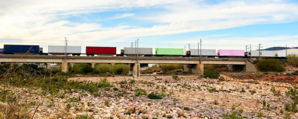 Güterzug mit Containern über trockenen Fluss als Folge von Niedrigwasser